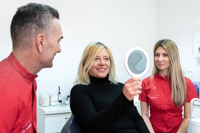 Dr. Jurisic and a female patient smile while looking at her new smile.